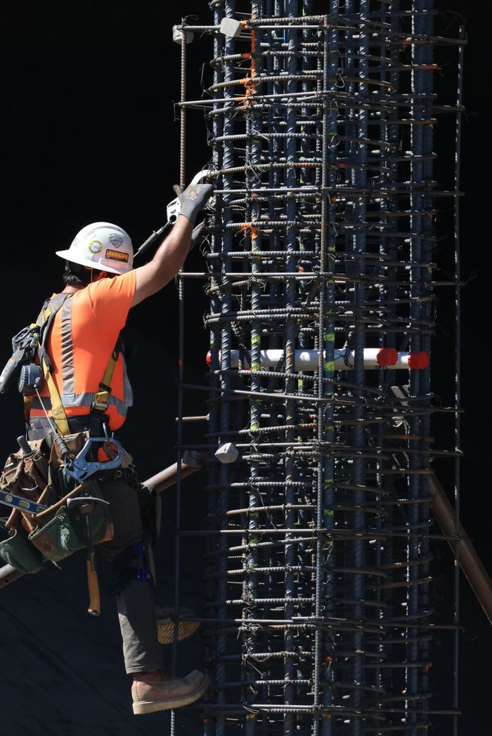 services-03 Worker in safety gear climbs a steel scaffolding structure on a construction site under daylight.