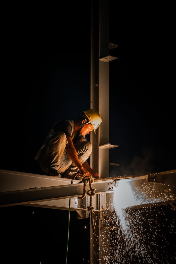 services-04 Industrial worker welding steel structure at night, casting bright sparks.