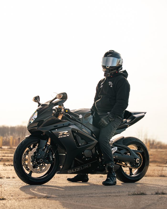 A biker sits on a sleek black Suzuki GSX-R motorcycle, basking in the golden outdoor light.