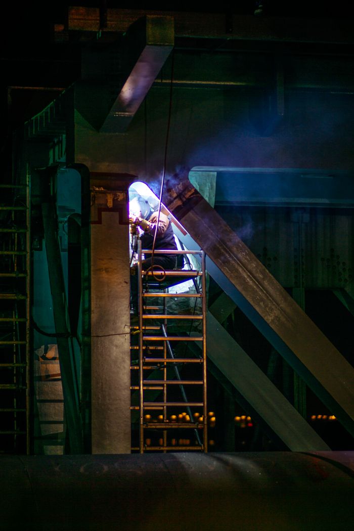 services-img A skilled welder operates on a large metal structure at night, producing bright sparks and smoke.