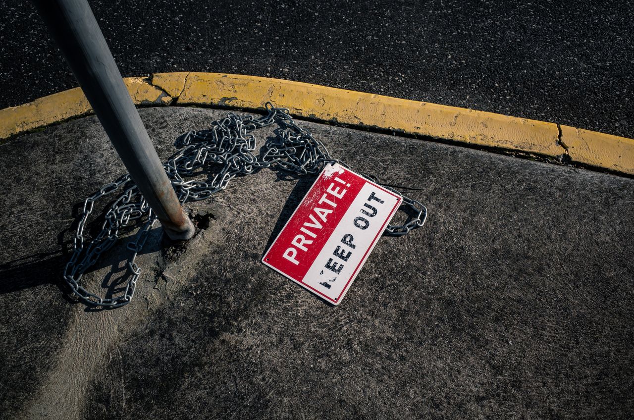 journey-01 A chained 'Private Keep Out' sign lies on an urban sidewalk, emphasizing security.
